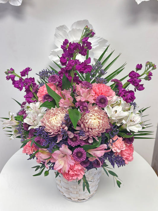 Bouquet of flowers with pink, purple, and white flowers in a basket on a white surface.