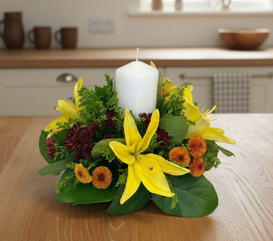 Floral arrangement with yellow lilies and a white candle on a table.