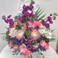 Bouquet of flowers with pink, purple, and white flowers in a basket on a white surface.