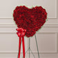 Heart-shaped arrangement of red flowers with a red bow in a store setting
