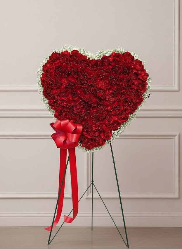 Heart-shaped arrangement of red flowers with a red bow in a store setting