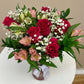 Bouquet of hot pink roses in a pink glass vase on a white surface.