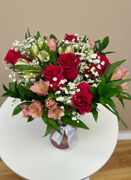 Bouquet of hot pink roses in a pink glass vase on a white surface.