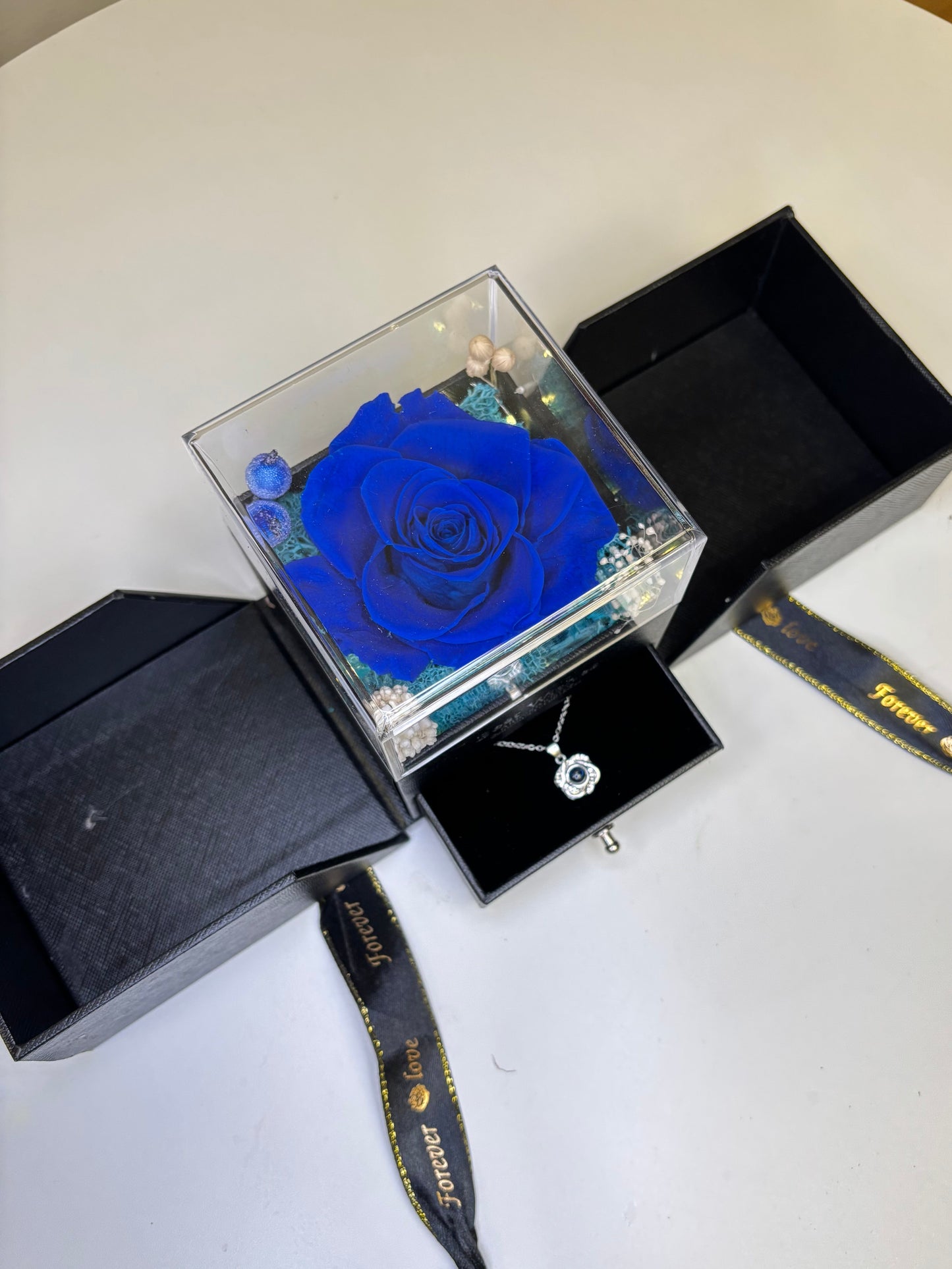 Blue rose in a transparent box with a necklace on a white surface